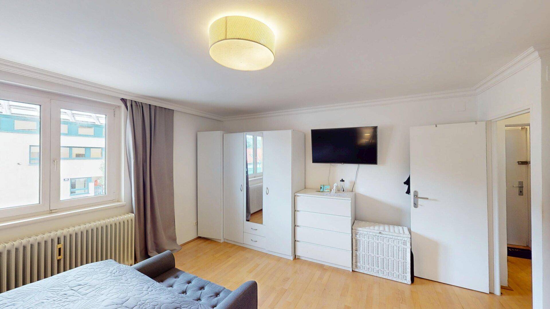 Helles Schlafzimmer mit Holzboden, Kommode und Blick nach draußen.
