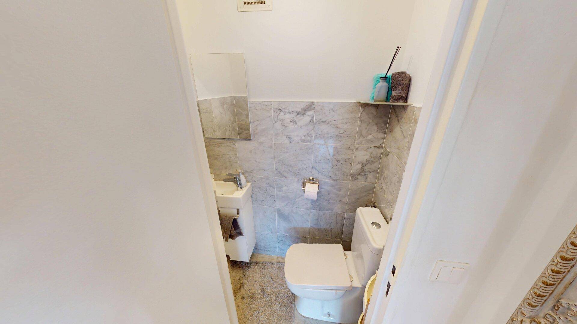 Kleines Gäste-WC mit Marmorfliesen und wandmontierter Toilette.