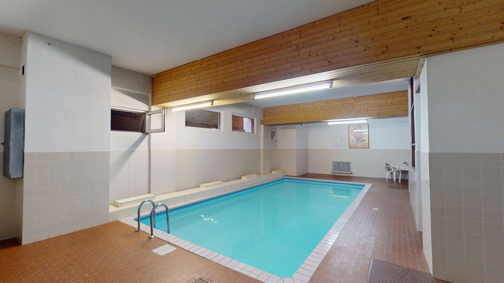 Innenpoolbereich mit gefliestem Becken und Holzdecke, ideal für Entspannung und Sport.