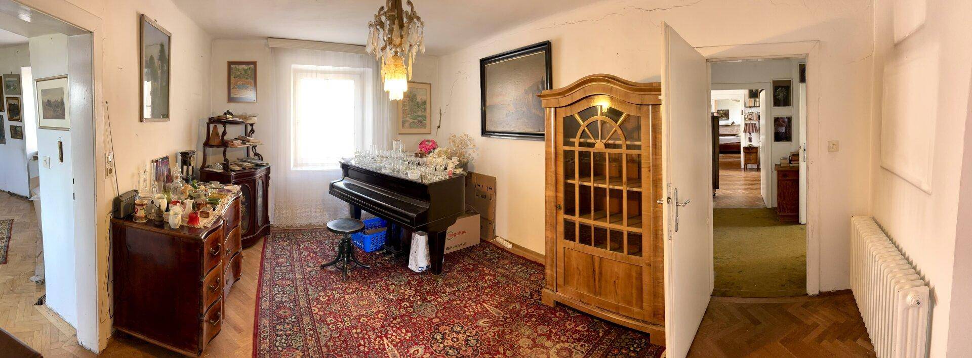 Helles Zimmer mit Teppichboden, antiken Möbeln und einem Klavier.