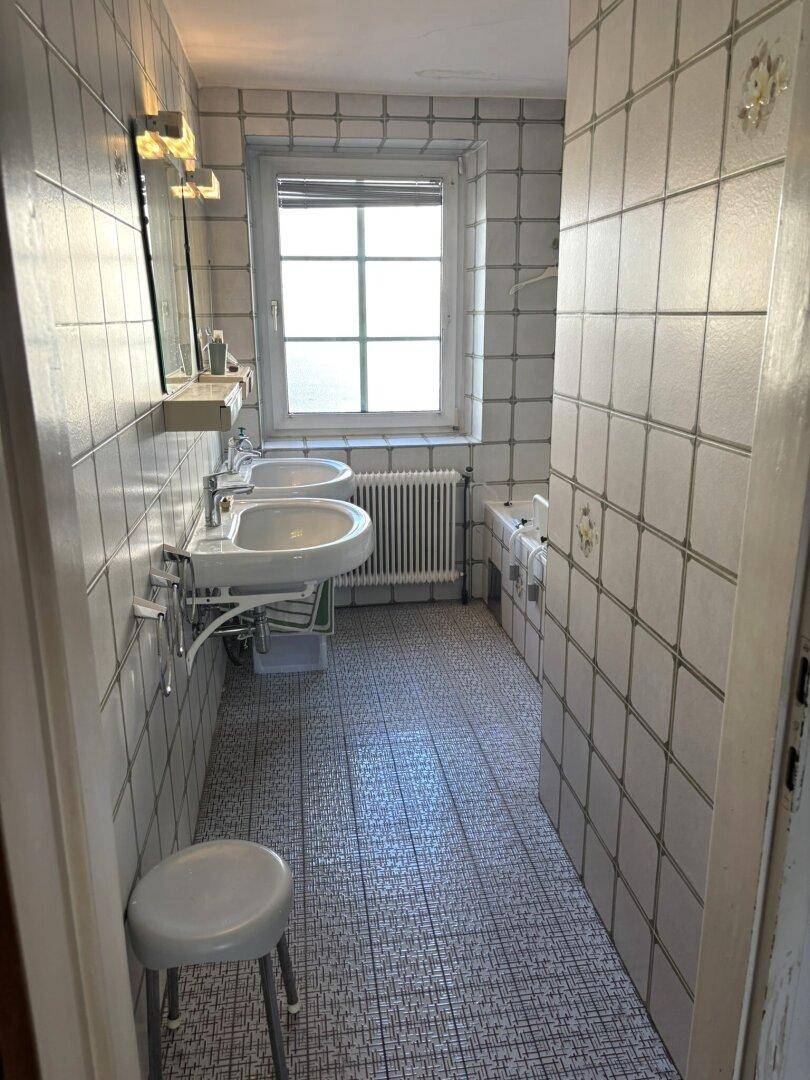 Badezimmer mit Doppelwaschbecken, Badewanne und Fenster, komplett gefliest.