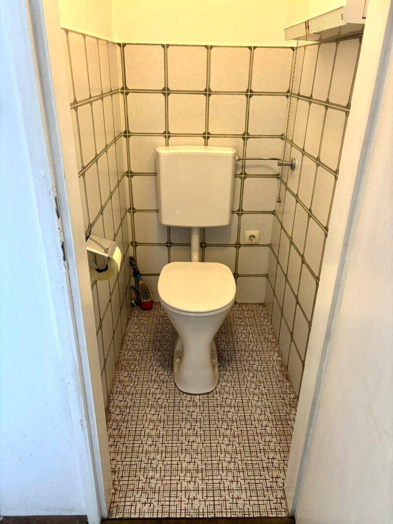 Separate Toilette mit WC und Fliesen an Wänden und Boden.