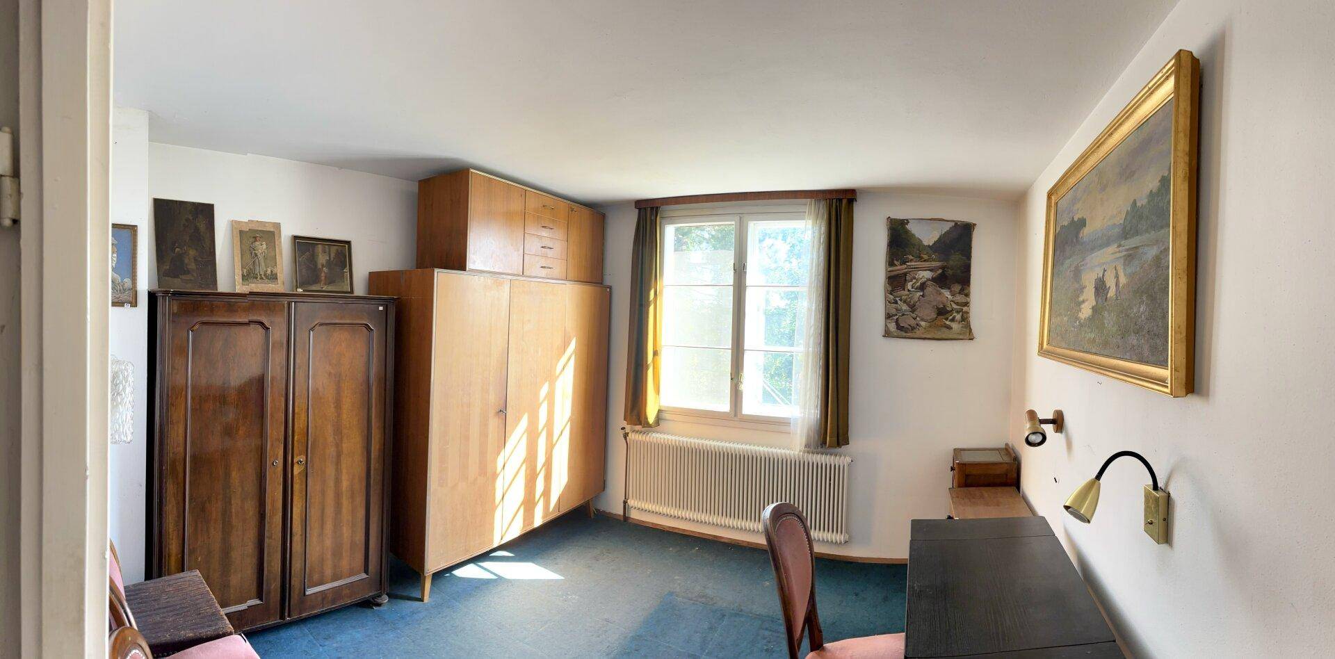 Schlafzimmer mit Teppichboden, Holzschränken und einem Fenster mit viel Tageslicht.