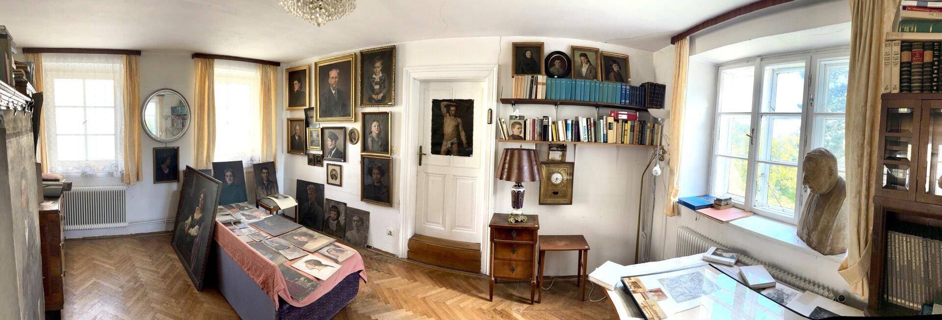 Arbeitszimmer mit vielen Büchern, Kunstwerken und einem Schreibtisch am Fenster.
