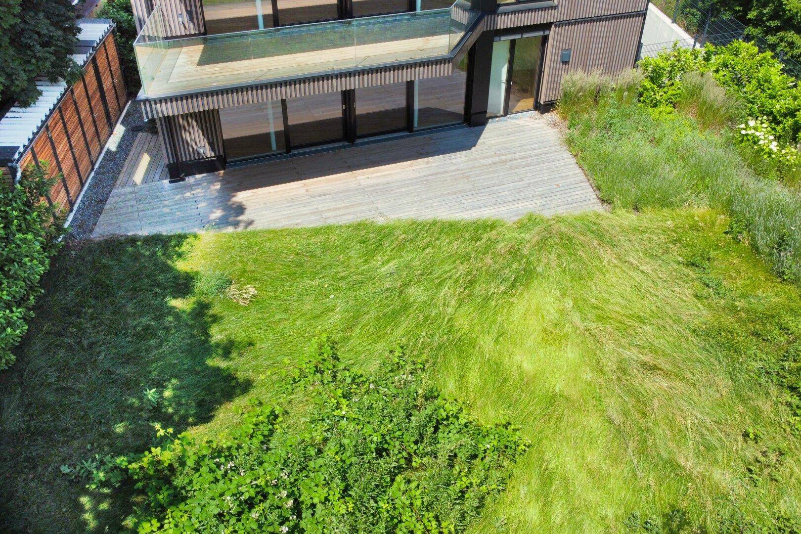 Vogelperspektive auf die grüne Gartenfläche und die Holzterrasse des modernen Gebäudes.