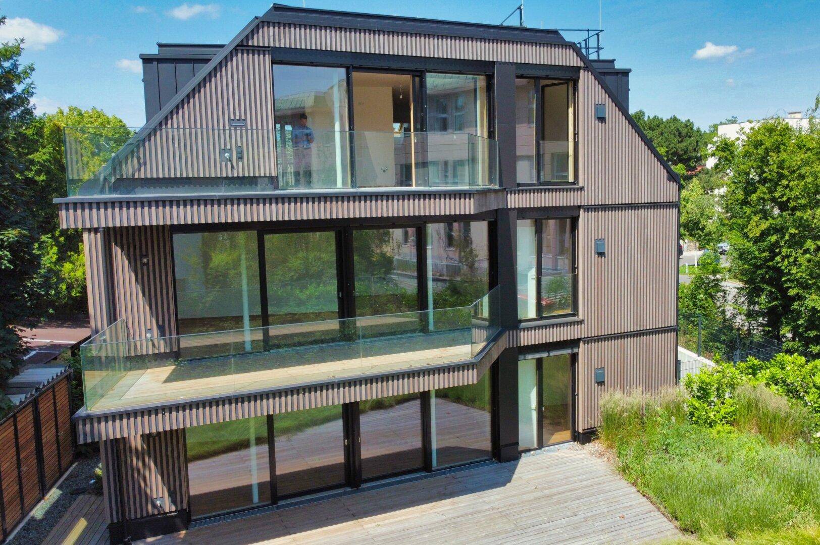 Ansicht der modernen Fassade mit vertikalen Holzlamellen und großen Glasfronten zu den Balkonen.