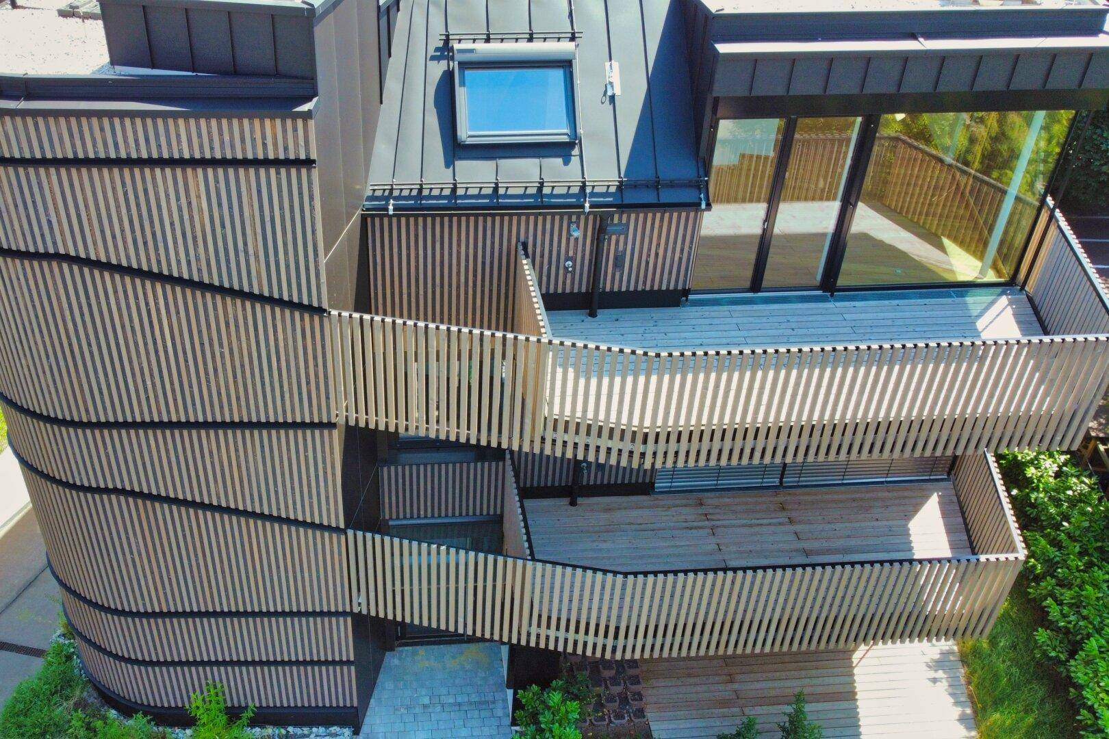 Seitenansicht des Gebäudes mit geschwungener Holzfassade und mehreren Balkonen.