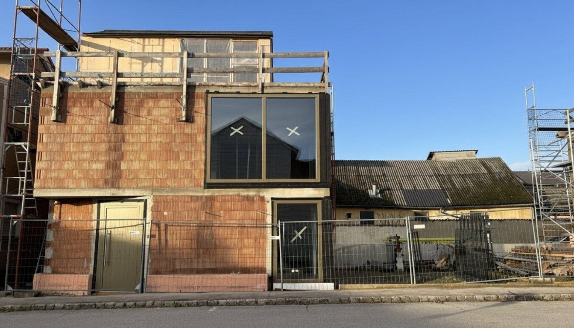 Fassade eines Neubaus im Rohbau mit großen Fenstern und angrenzendem älteren Gebäude.