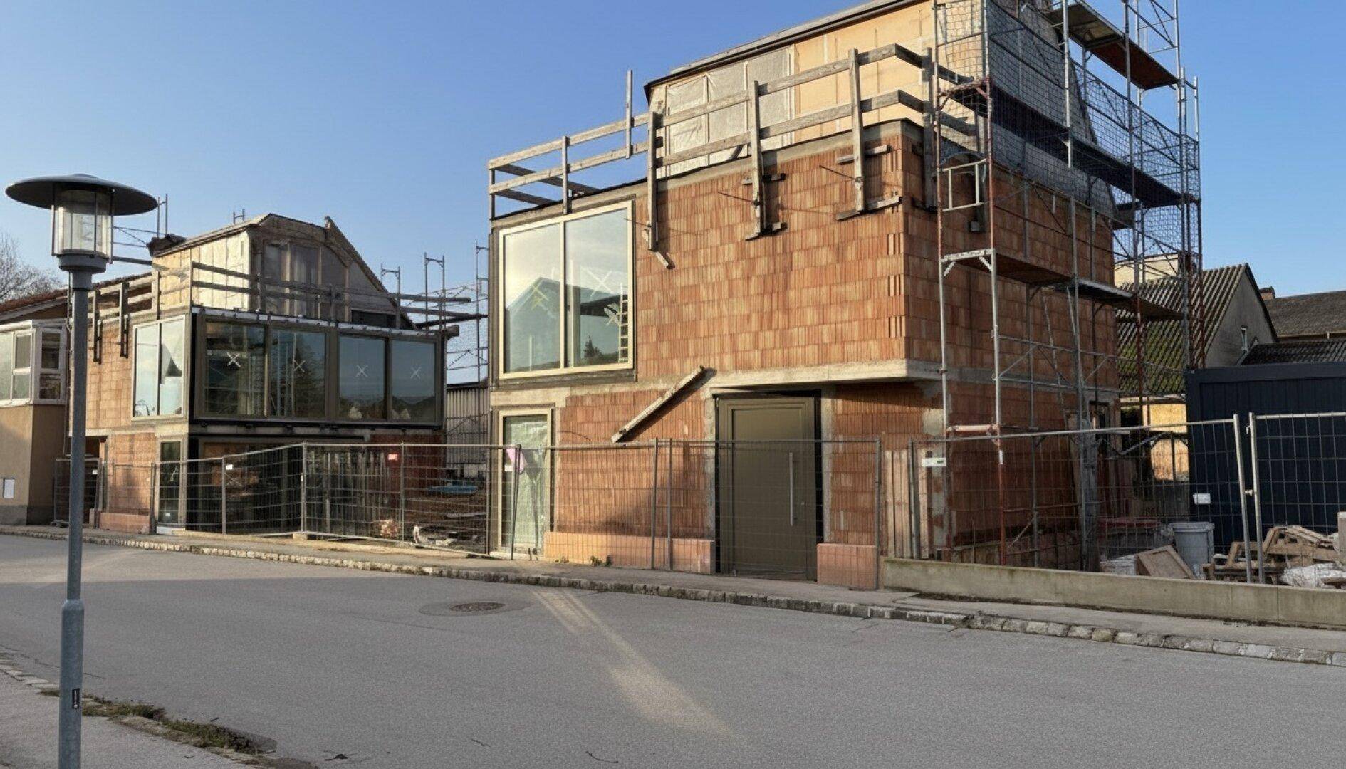 Zwei Neubauten im Rohbau mit Gerüst und großen Fensterflächen an einer ruhigen Straße.