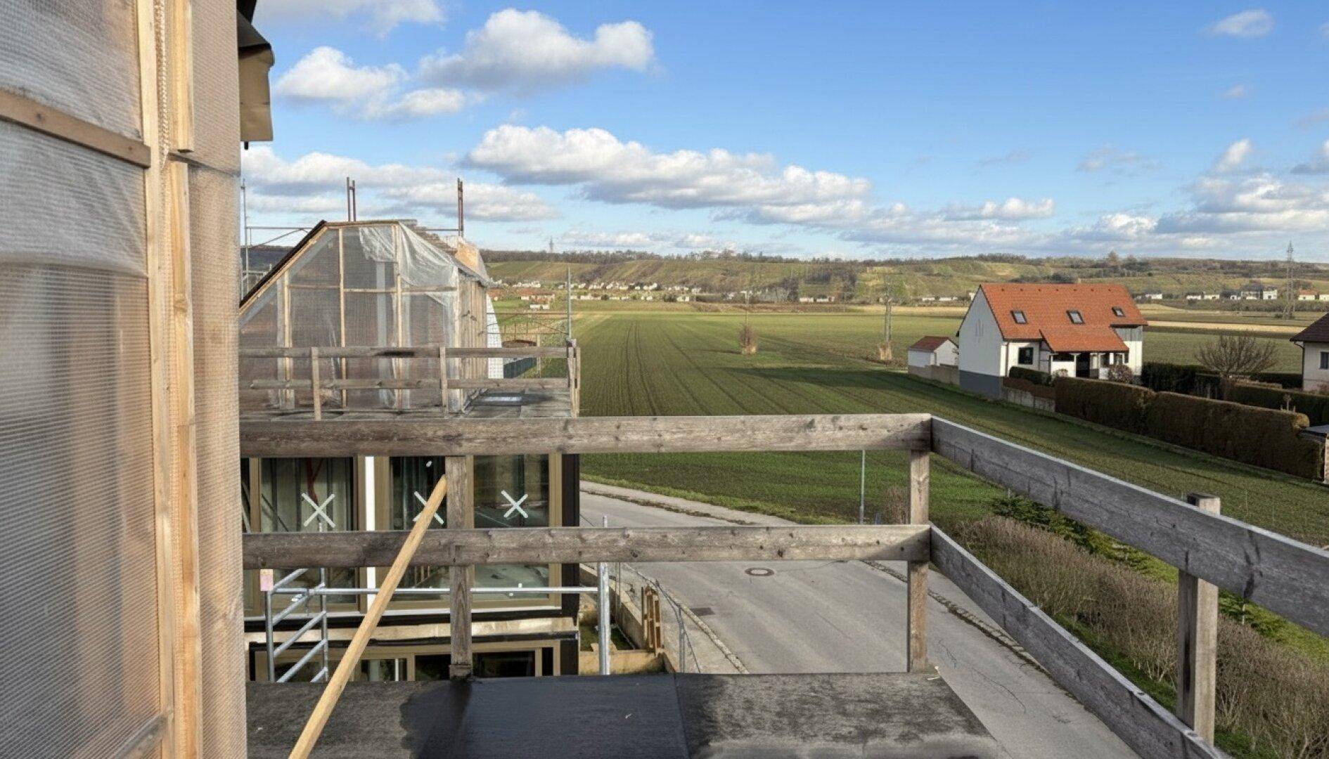 Unfertige Terrasse mit Holzzaun und weitem Blick über Felder und die ländliche Umgebung.