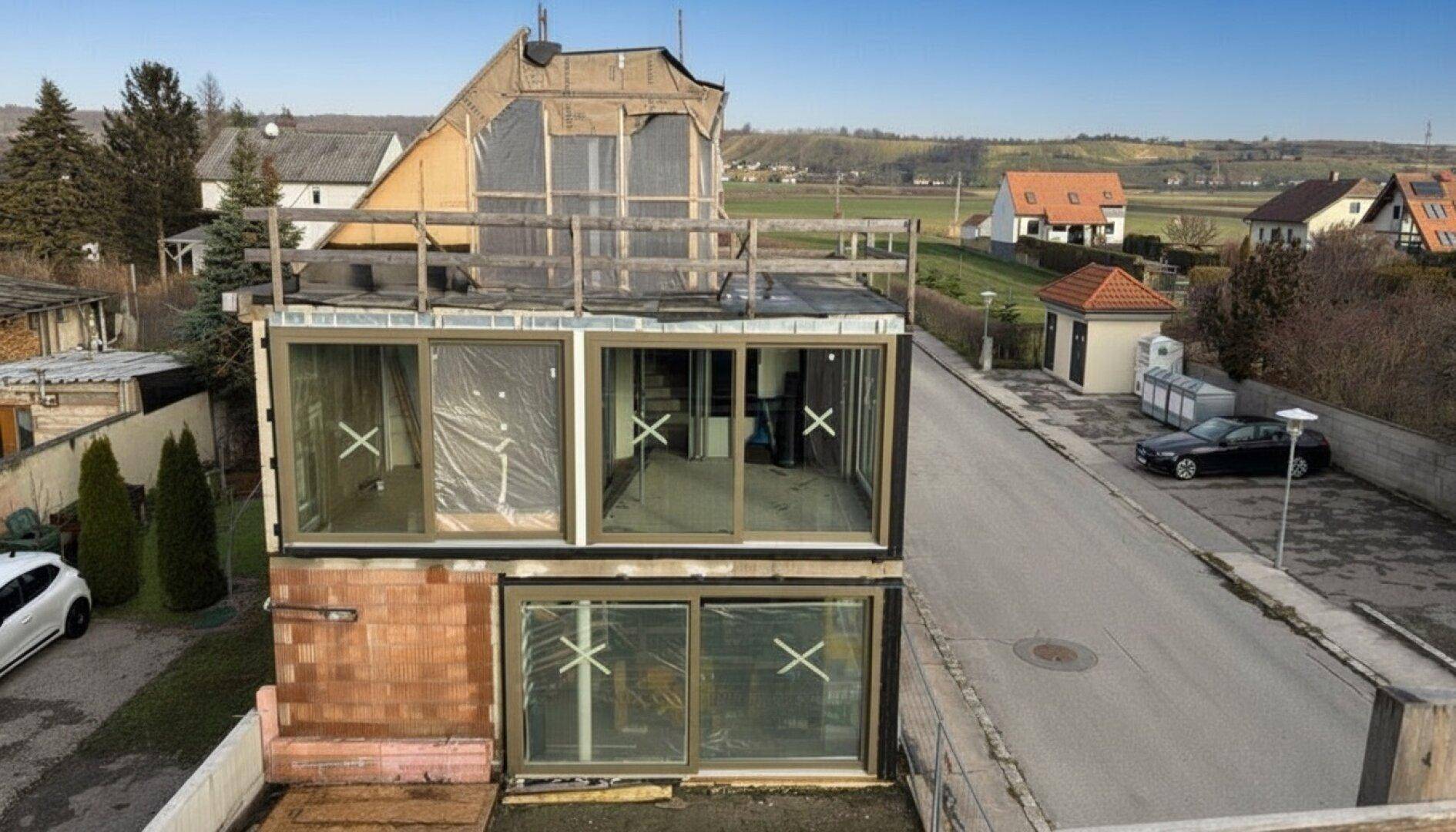 Luftaufnahme eines im Bau befindlichen Hauses mit großen Fenstern und Blick auf die Straße und Landschaft.