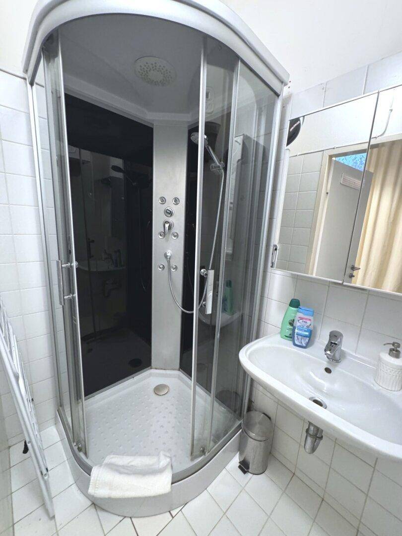 Modernes Badezimmer mit Duschkabine, Waschbecken und Spiegelschrank, alles in Weiß gehalten.