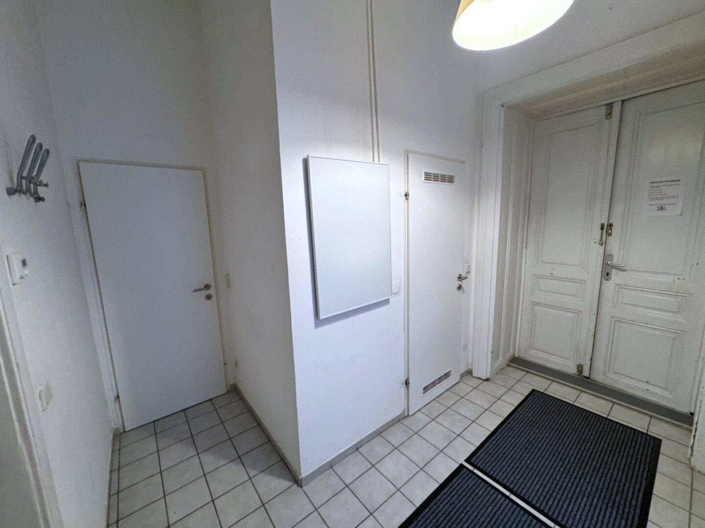 Eingangsbereich mit weiß gestrichenen Wänden, Fliesenboden und zwei Türen, die zu den Zimmern führen.