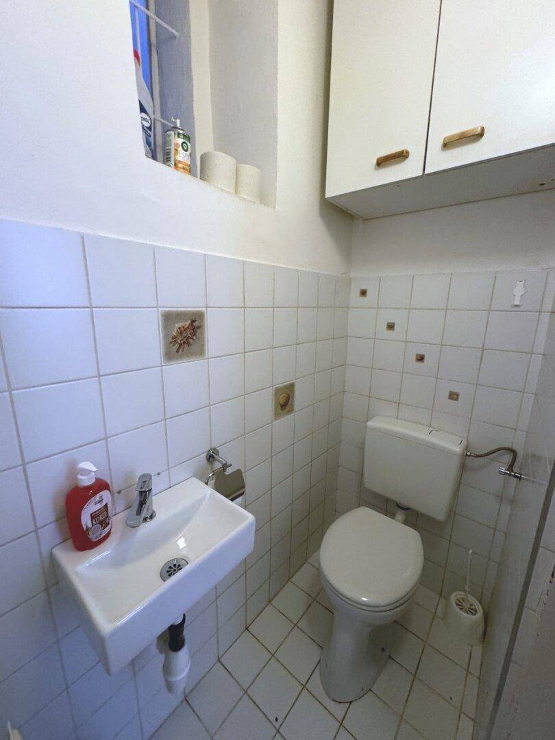 Kleines Gäste-WC mit Toilette, Waschbecken und einem Fenster für natürliche Belüftung.