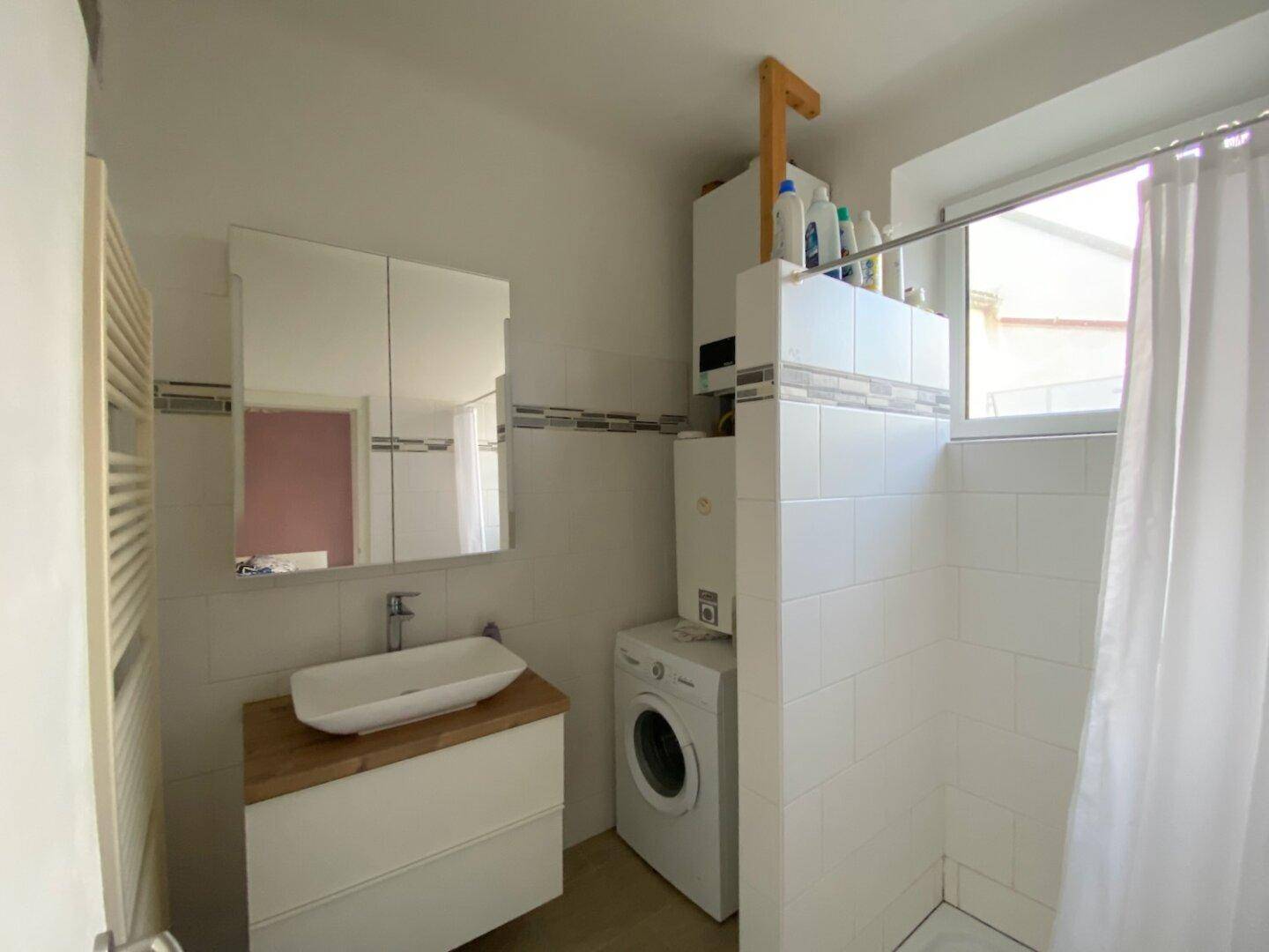 Helles Badezimmer mit Waschbecken, Spiegelschrank, Waschmaschine und Fenster.