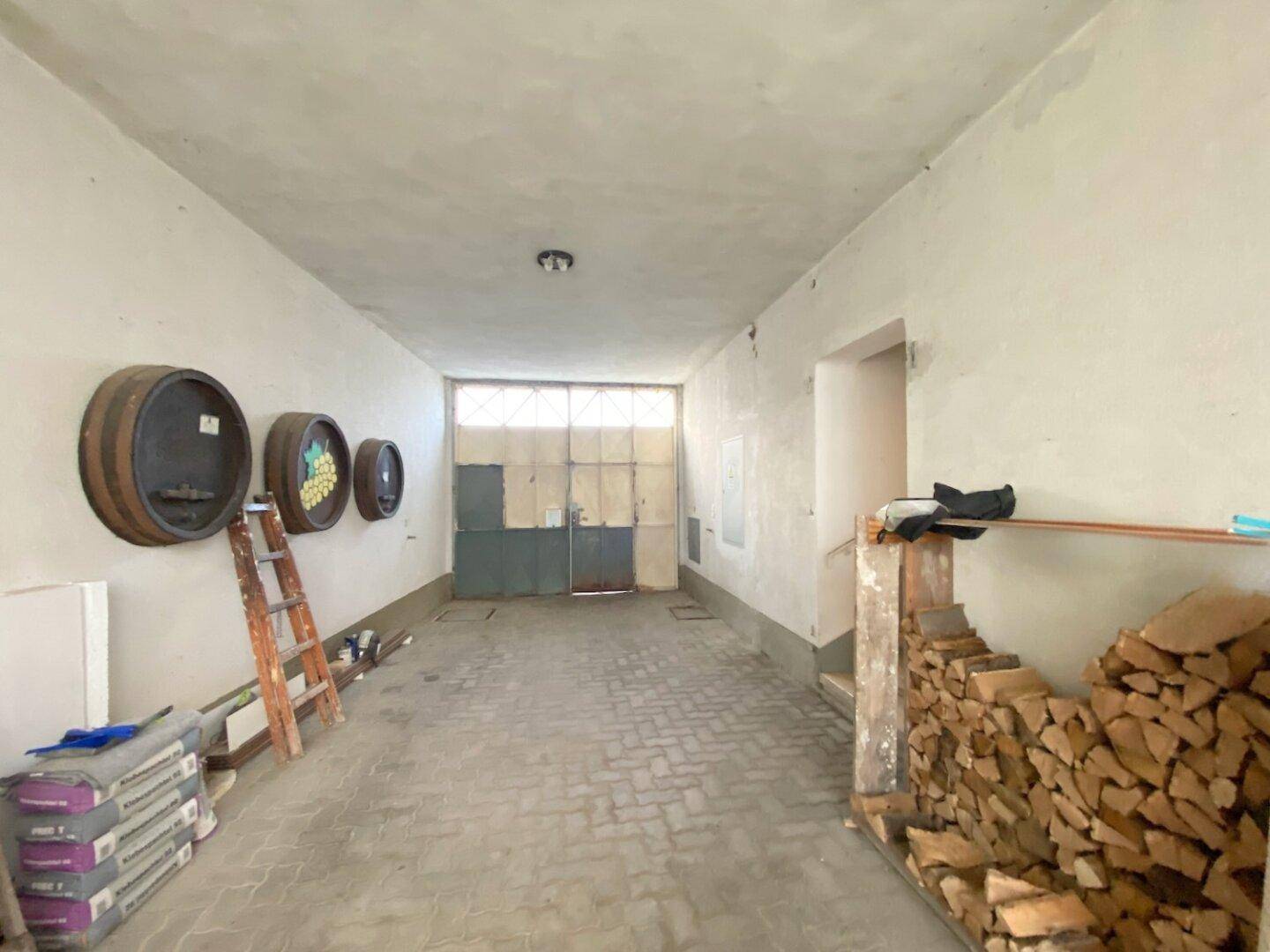 Geräumiger Lagerraum oder Garage mit Holzfässern und einem Stapel Brennholz.
