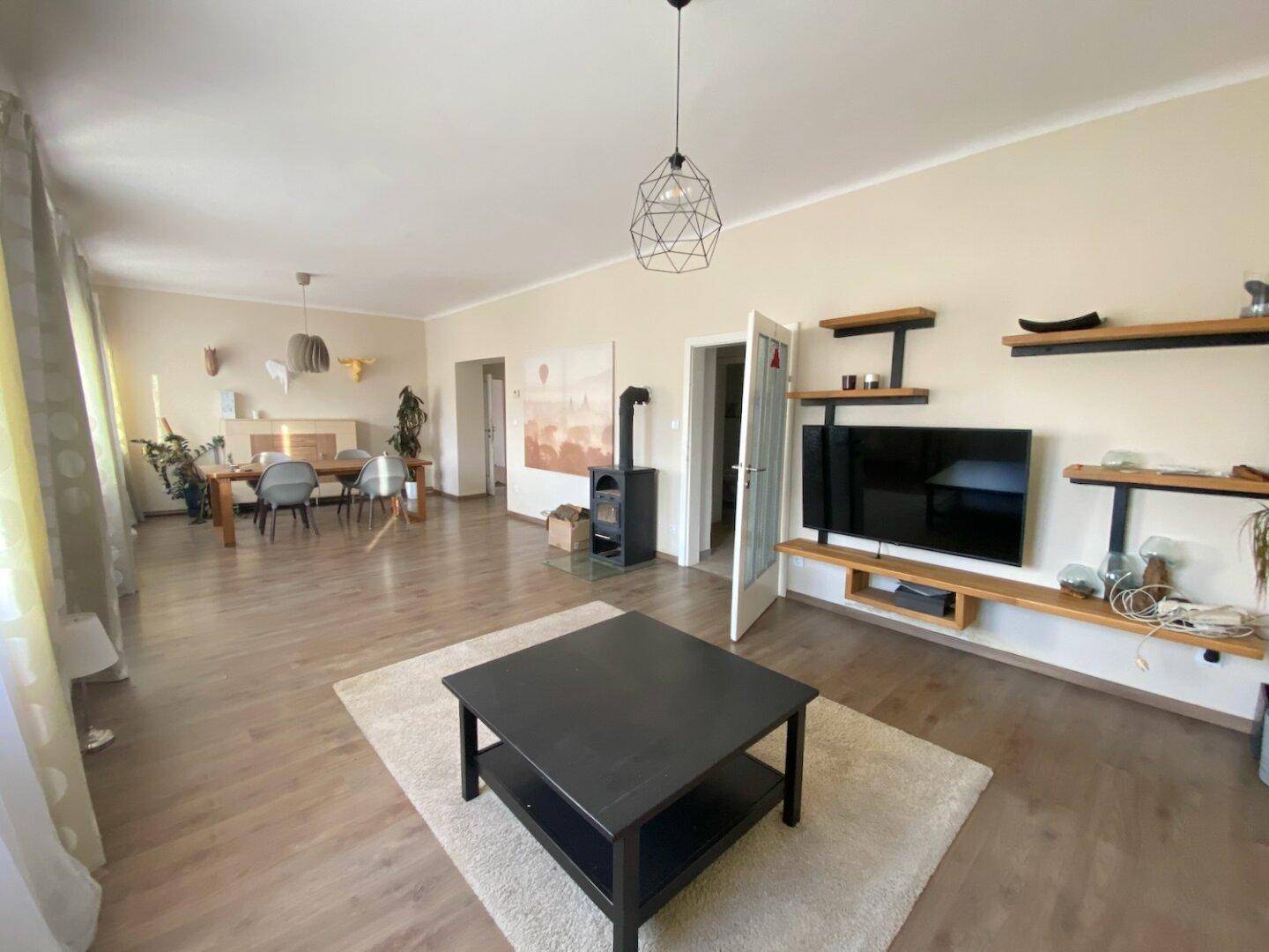 Gemütlicher Wohn-Essbereich mit Holzboden, Kaminofen und modernen Regalen an der Wand.