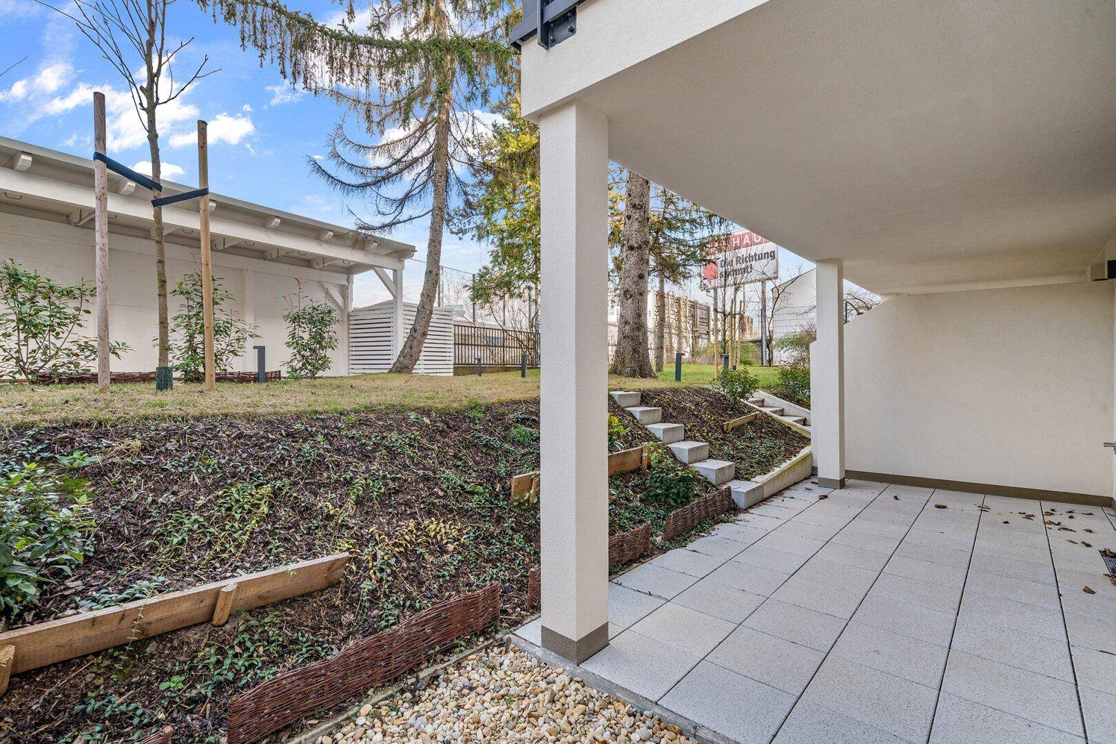 Überdachte Terrasse mit Fliesenboden und Blick auf den leicht erhöhten Gartenbereich.