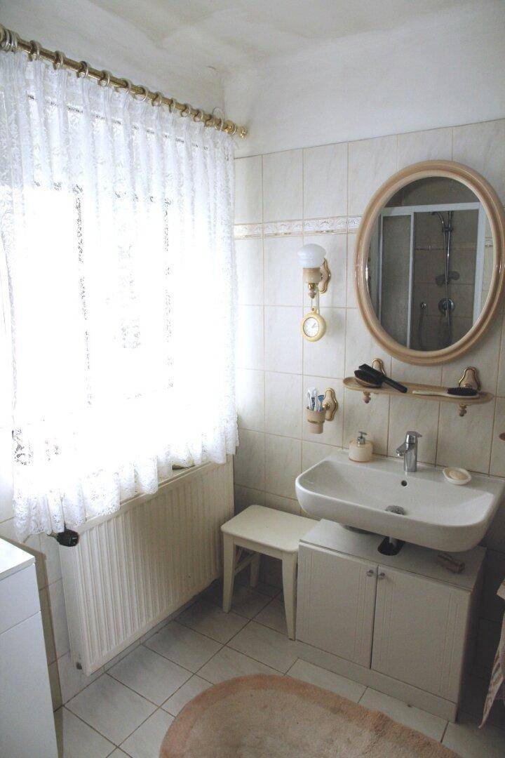 Funktionales Badezimmer mit Waschbecken, Spiegel und Fenster, hell gefliest und gut beleuchtet.