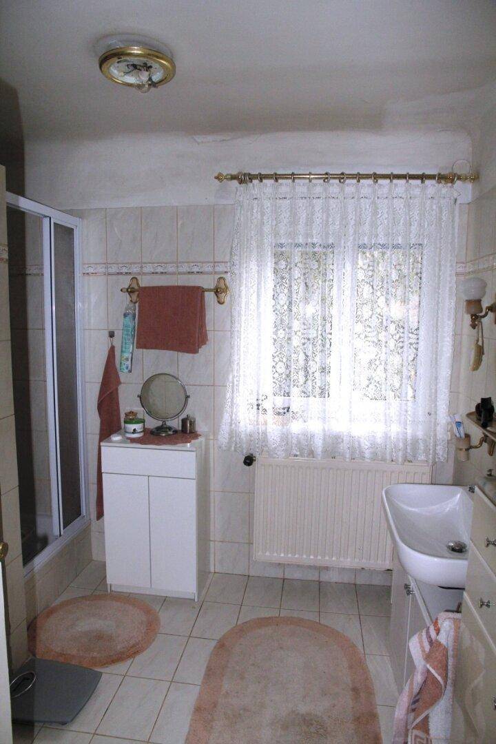 Helles Badezimmer mit Dusche, Waschbecken und Fenster, ausgestattet mit hellen Fliesen.