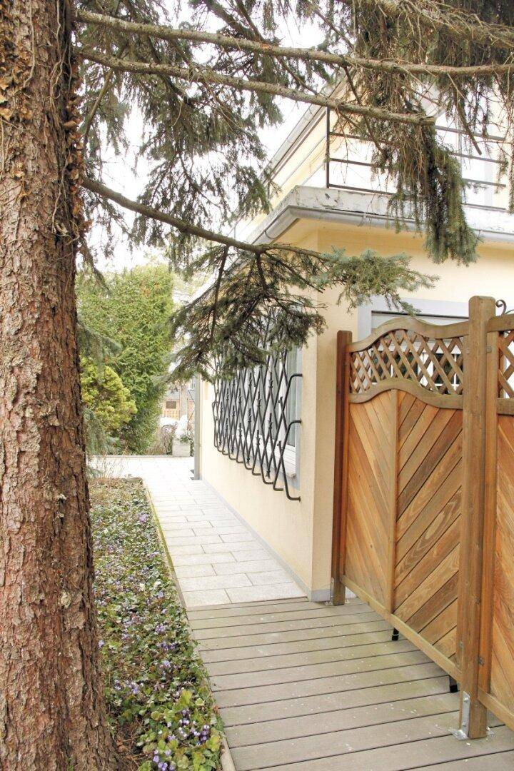 Seitlicher Zugang zum Haus mit Holzweg und gepflegter Bepflanzung.