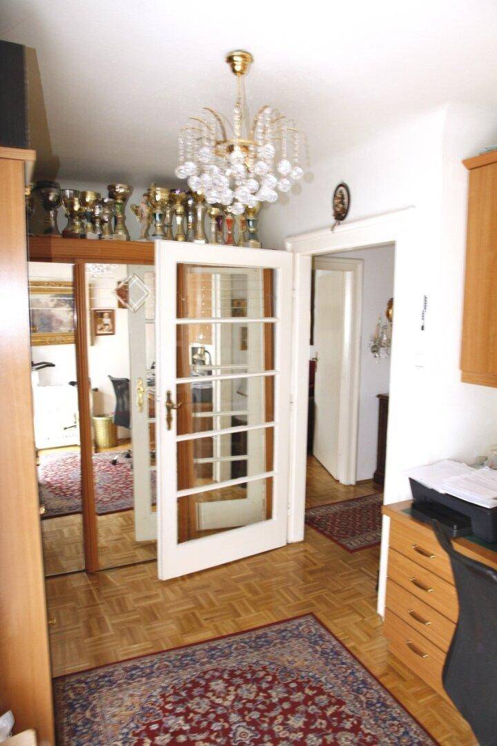 Heller Flur mit Parkettboden, Spiegelschrank und Kronleuchter, der zu weiteren Räumen führt.