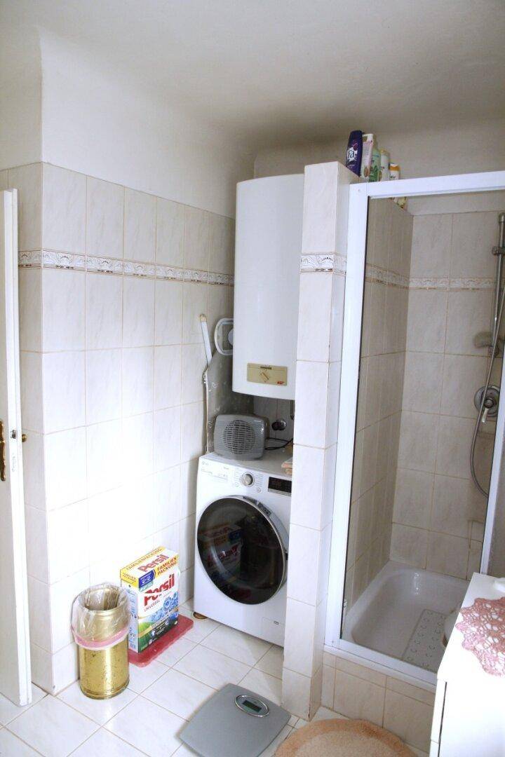 Badezimmer mit Duschkabine und Boiler, praktisch eingerichtet mit hellen Fliesen.