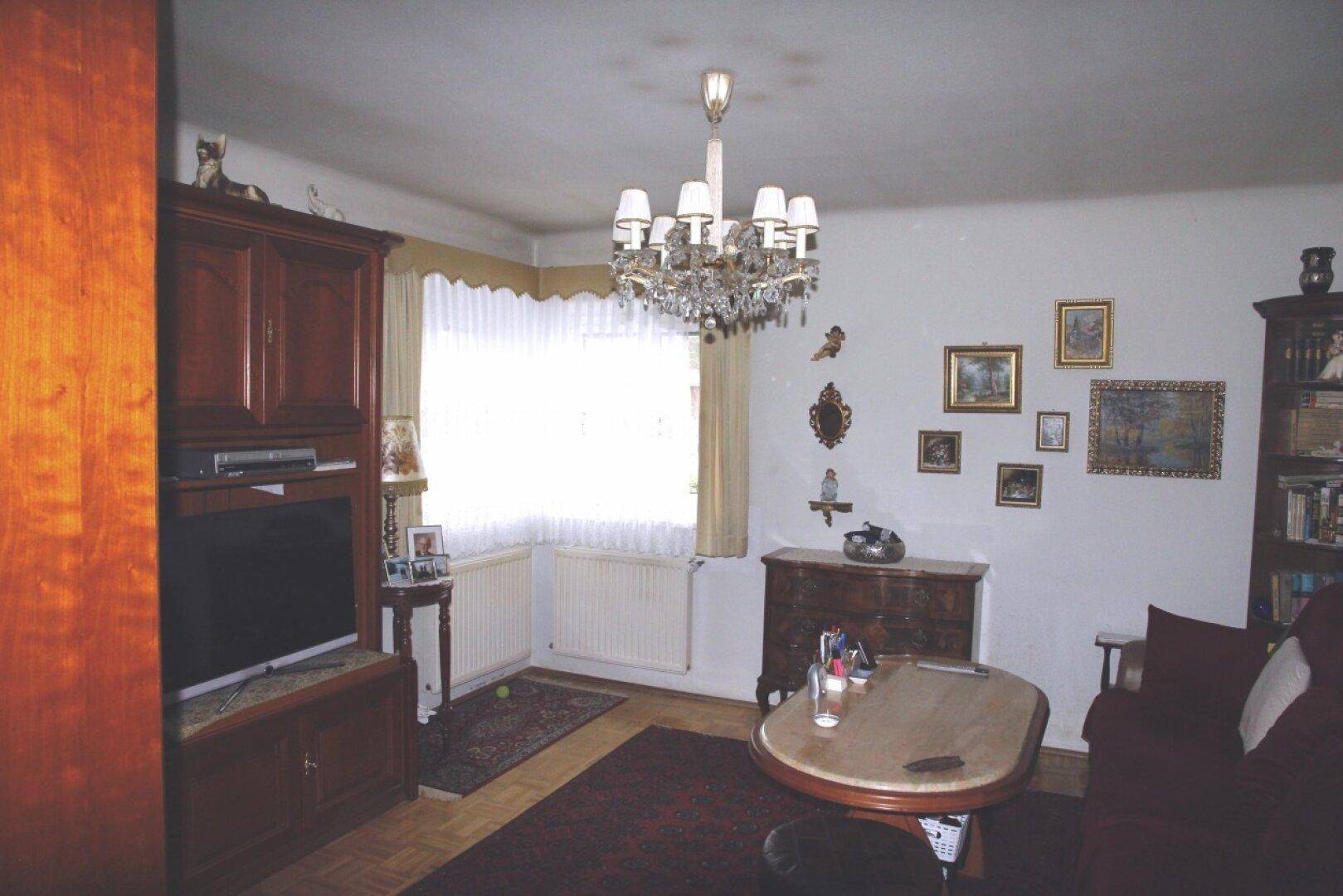 Helles Wohnzimmer mit Parkettboden, Fernsehmöbeln und einem großen Fenster.