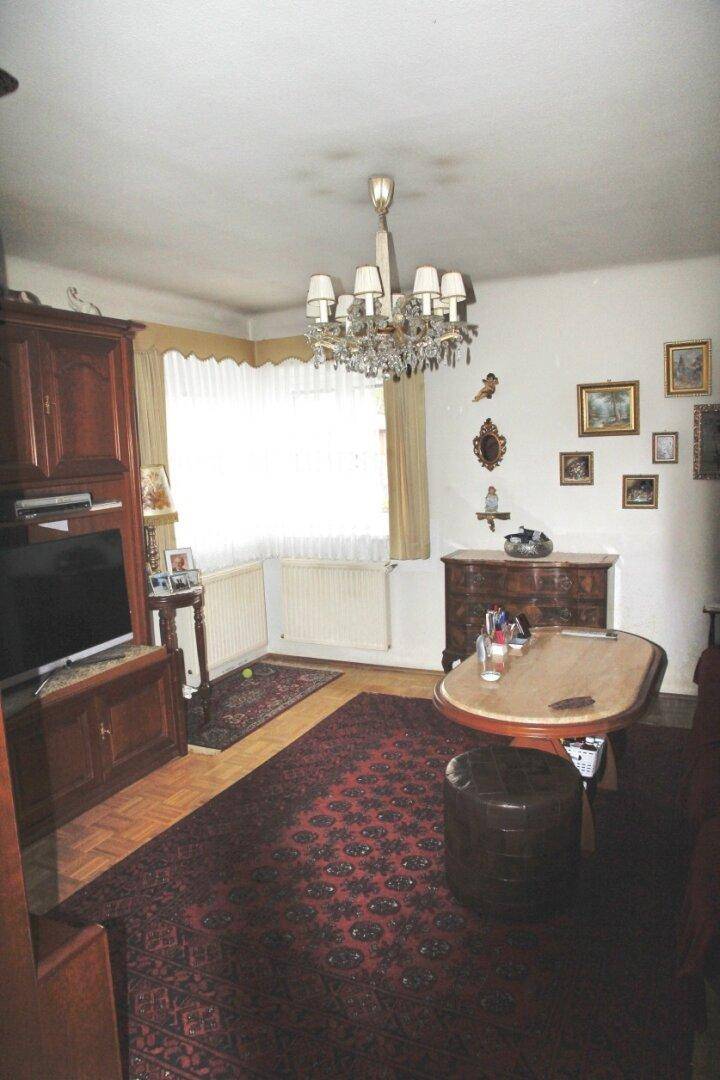 Gemütliches Wohnzimmer mit Parkettboden, Fernseher und klassischem Kronleuchter.