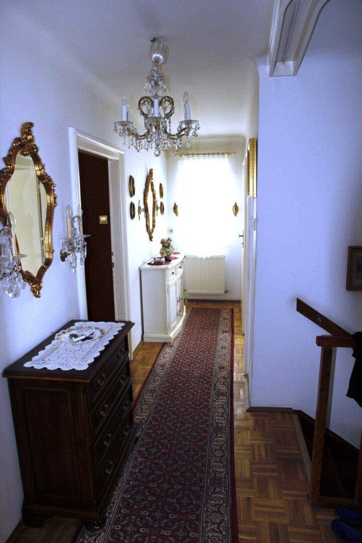 Heller Flur mit Parkettboden, eleganten Spiegeln und Kronleuchter, der zu den Zimmern führt.