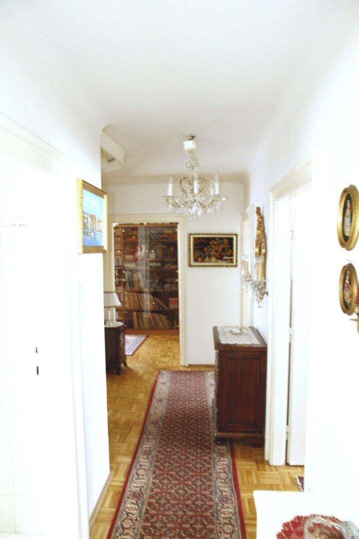 Langer, heller Flur mit Parkettboden und Kronleuchter, der einen Blick in ein weiteres Zimmer bietet.