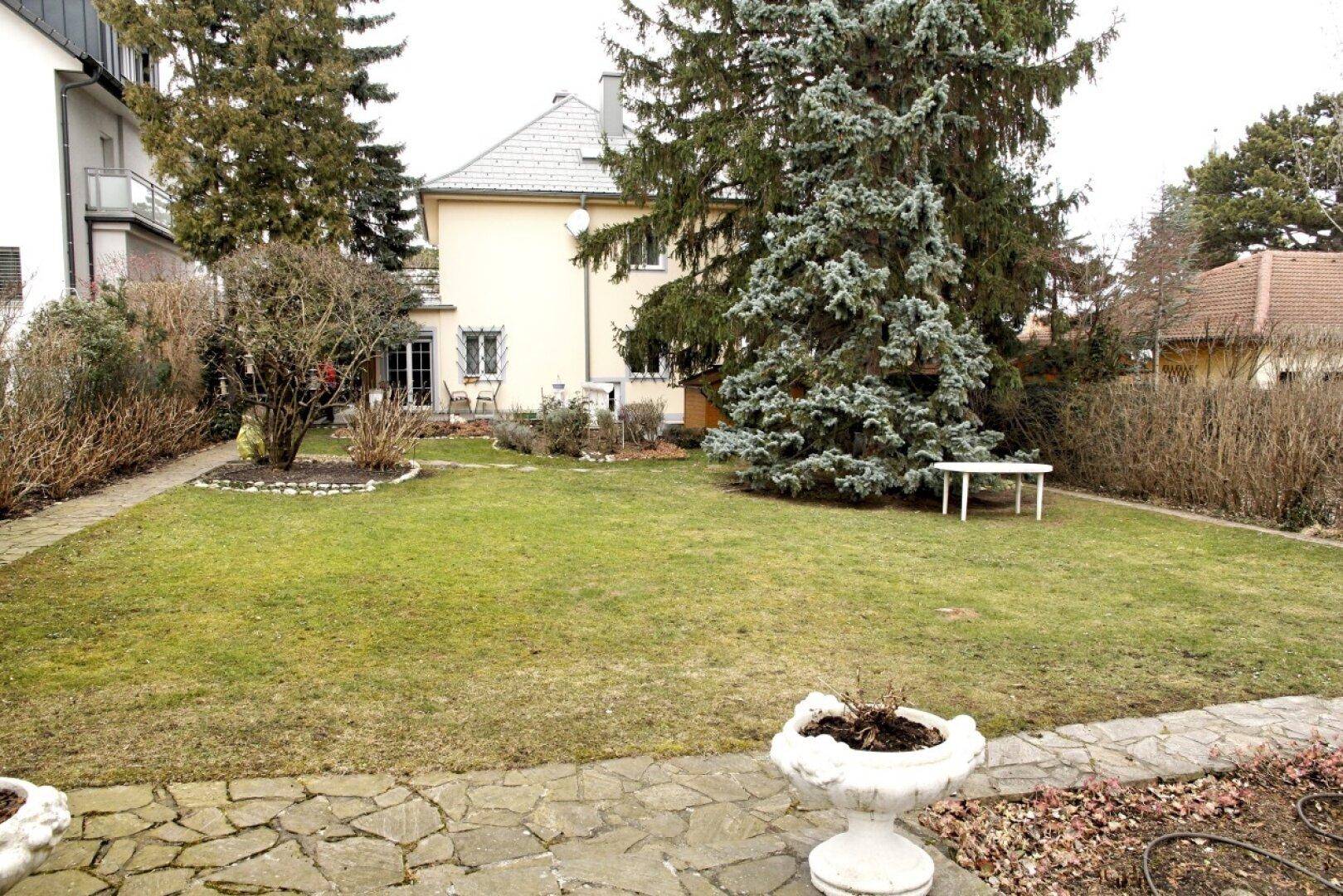 Großer, sonniger Garten mit Rasenfläche und einem charmanten Einfamilienhaus im Hintergrund.