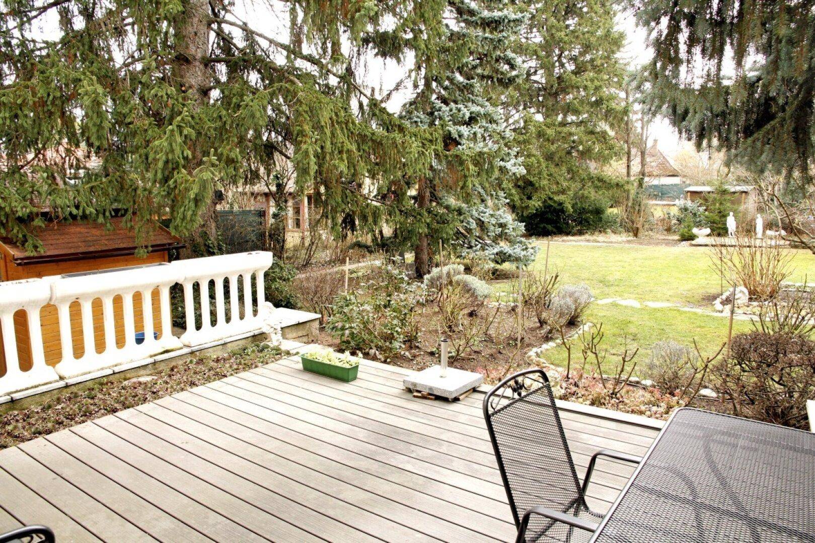 Geräumige Holzterrasse mit Gartenmöbeln und Blick auf den gepflegten Gartenbereich mit Bäumen.