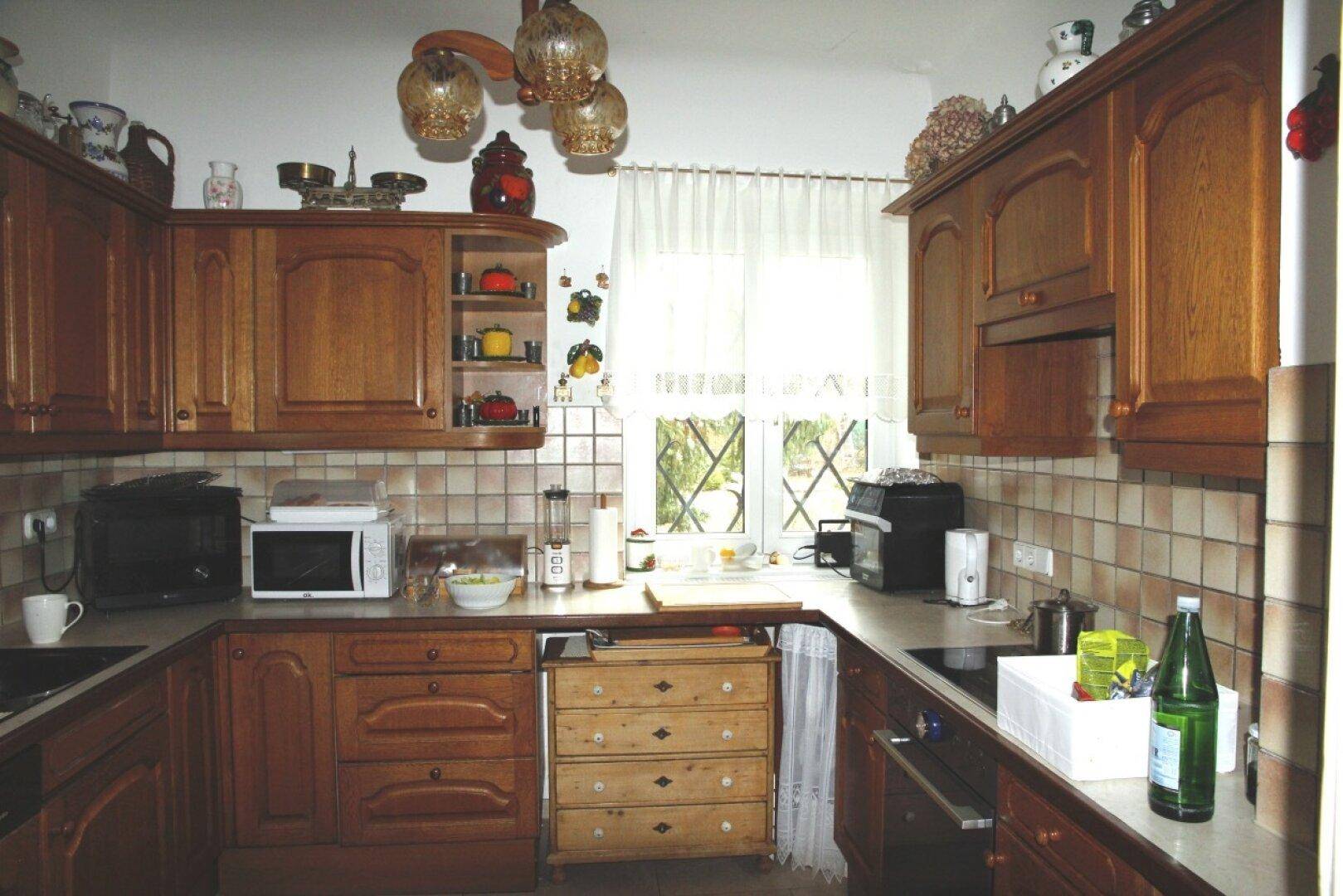 Traditionelle Holzküche mit Einbauschränken, Fliesenrückwand und Fenster mit Blick ins Grüne.
