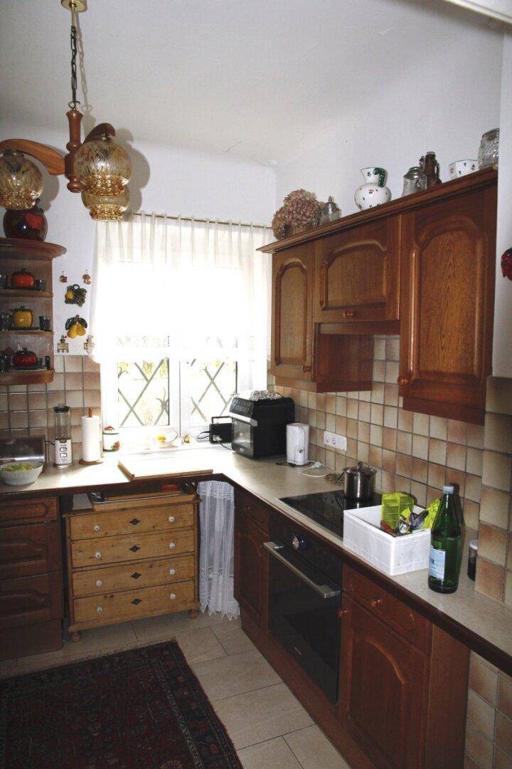 Funktionale Küche mit Holzschränken, integriertem Backofen und hellem Fensterbereich.
