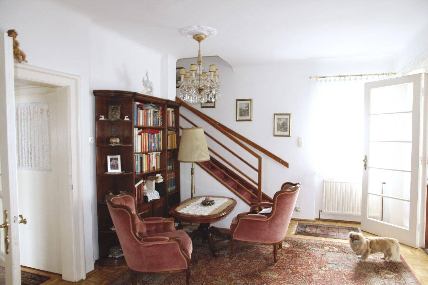 Eingangsbereich mit Holztreppe, Bücherregal und zwei bequemen Sesseln, klassisch eingerichtet.