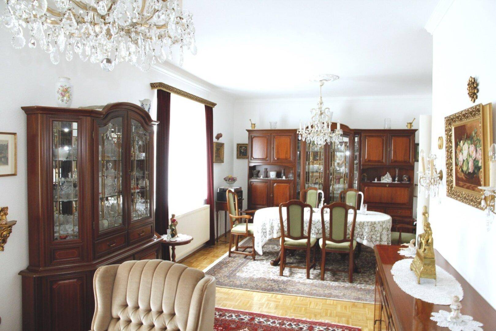 Klassischer Wohn-Essbereich mit eleganten Holzmöbeln, Kronleuchtern und traditionellem Teppichboden.