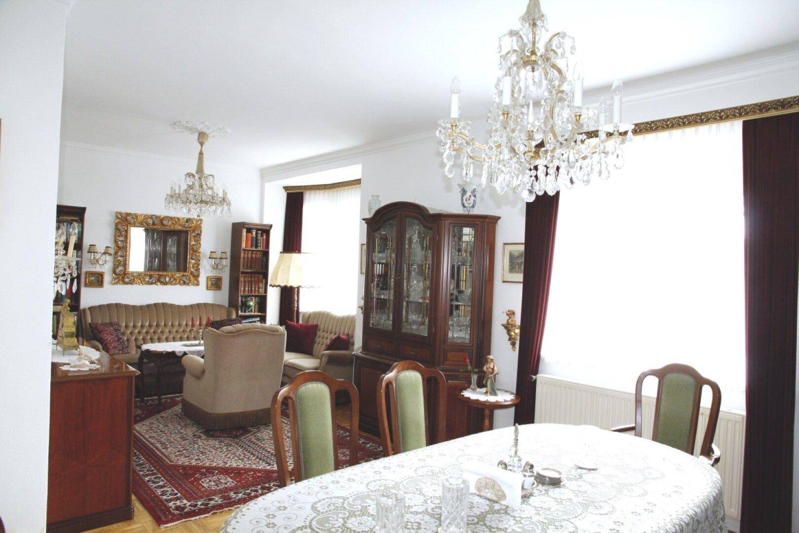 Geräumiger Wohn-Essbereich mit klassischem Interieur, dunklen Holzmöbeln und opulenten Kronleuchtern.