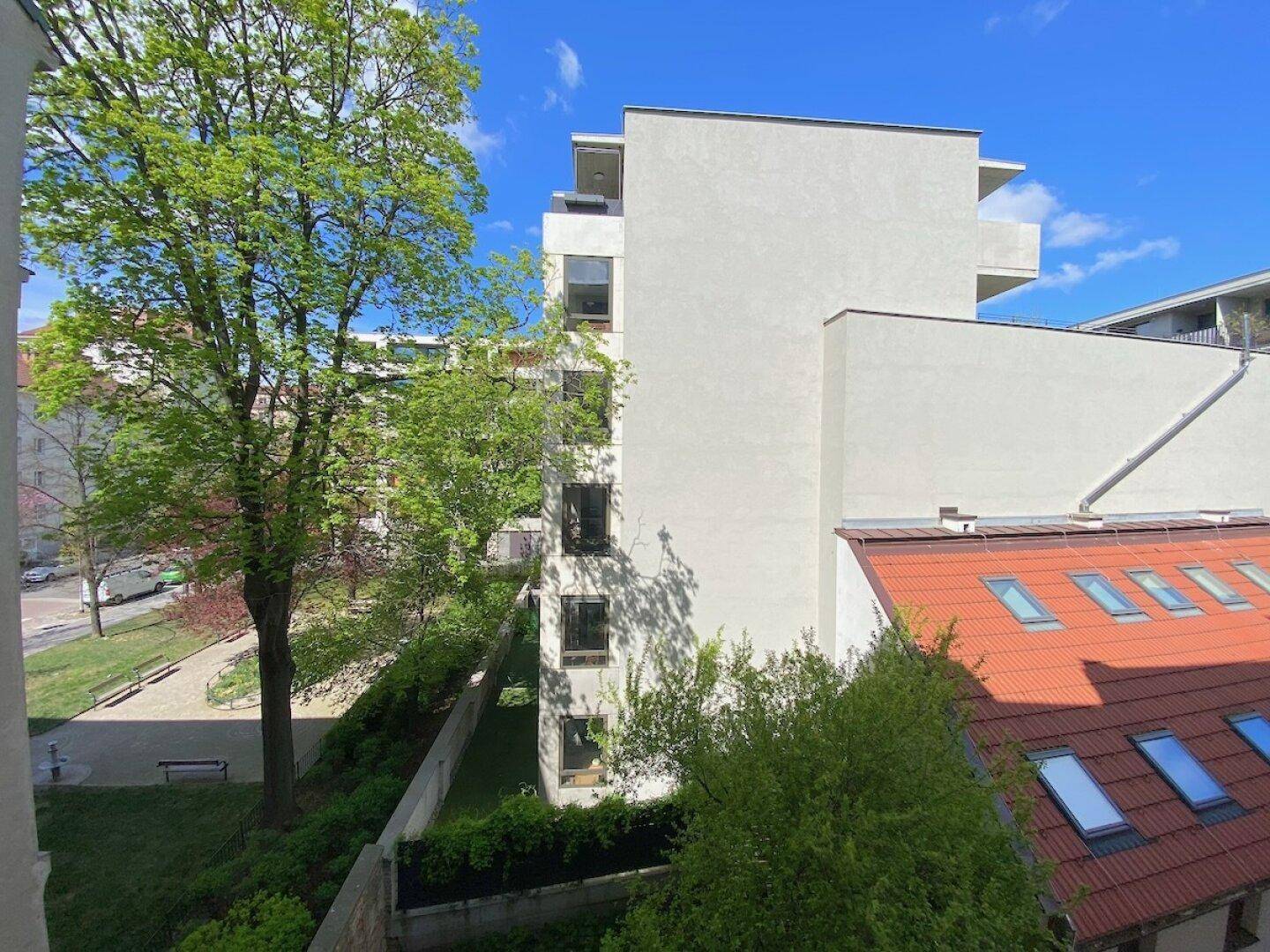Aussicht von einem Balkon auf ein modernes Gebäude, grüne Bäume und ein Dach mit Dachfenstern.