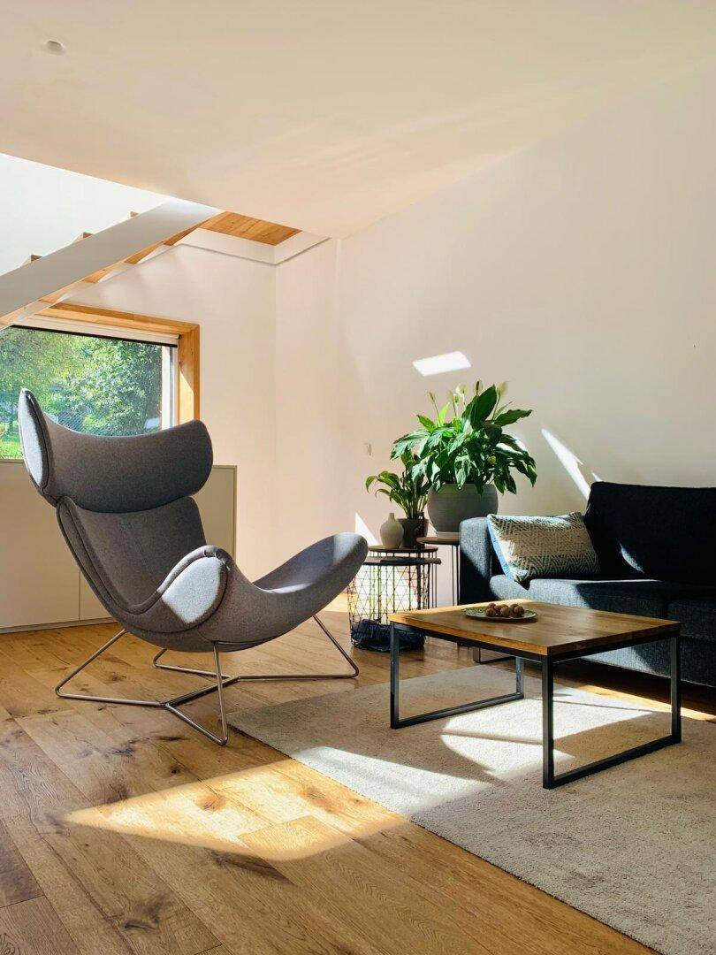 Sonniges Wohnzimmer mit bequemen Sitzmöbeln, Holzboden und grünen Zimmerpflanzen.