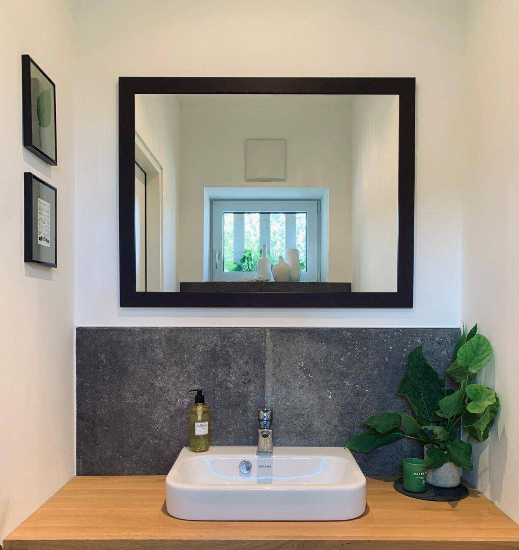 Modernes Gäste-WC mit Einzelwaschbecken, Holzplatte und einem großen Wandspiegel.