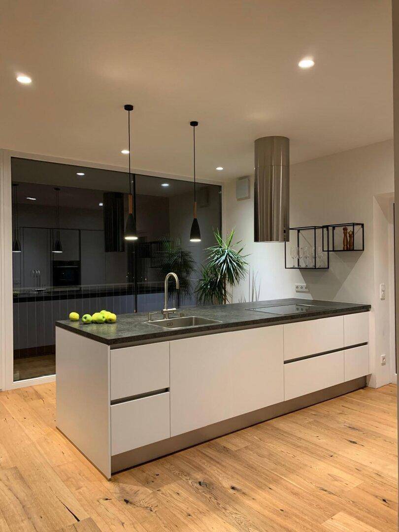 Elegante Kücheninsel mit minimalistischem Design und großen Fensterfronten, die viel Licht hereinlassen.