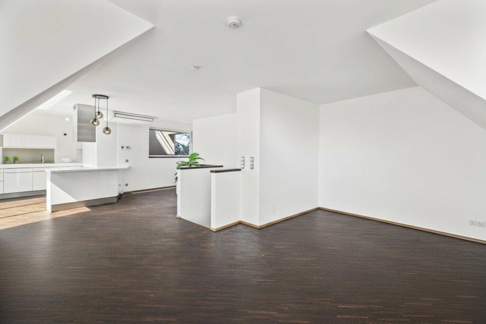 Offener Wohnbereich mit Dachschrägen, dunklem Holzboden und Blick auf die integrierte moderne Küche.