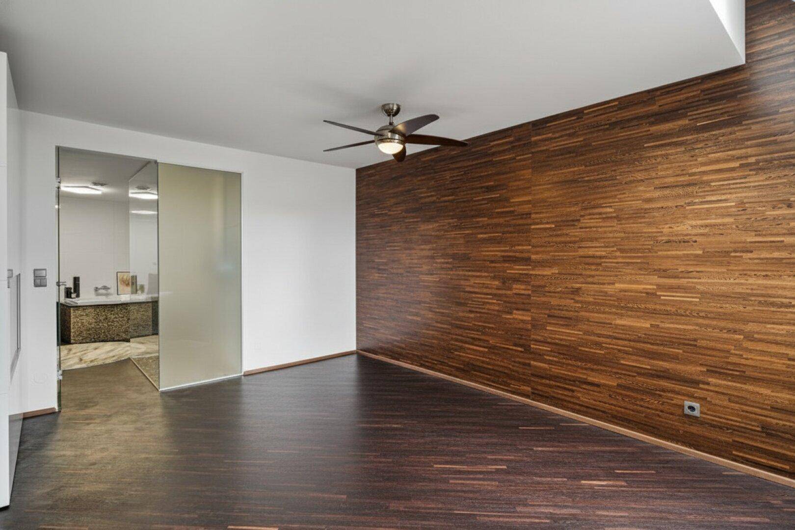 Schlafzimmer mit Holzwand, dunklem Holzboden und Zugang zu einem modernen Badezimmer.