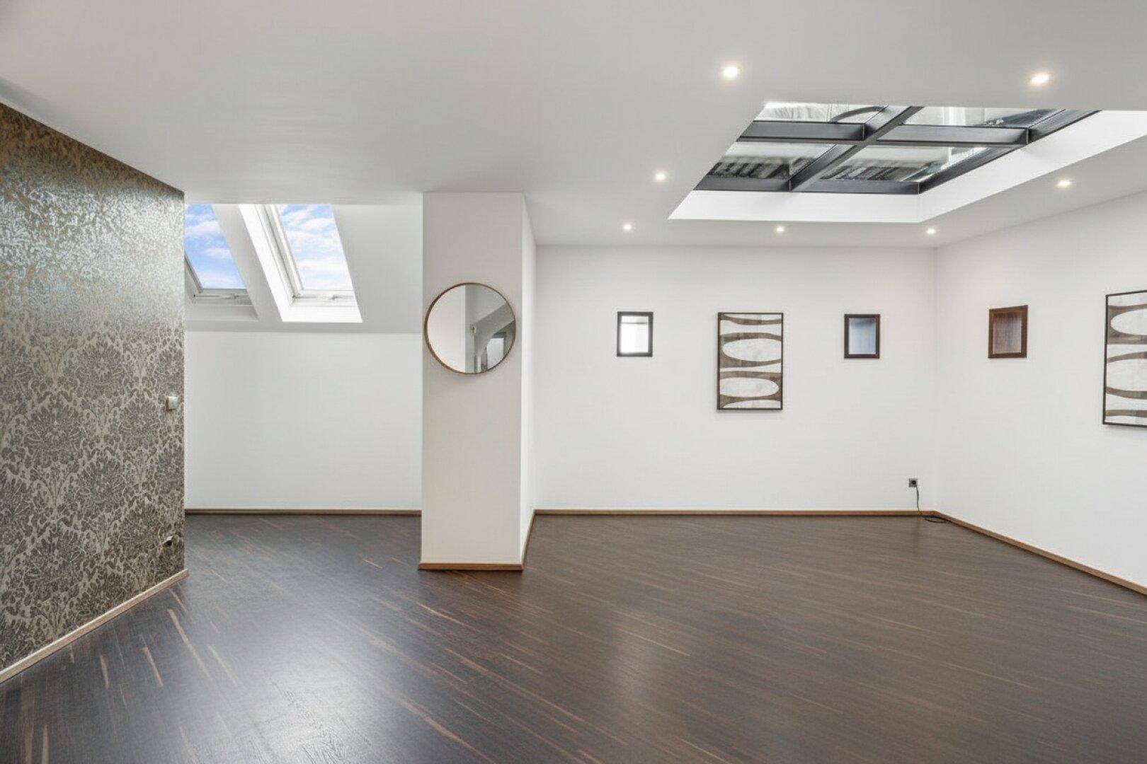 Heller Wohnraum mit dunklem Holzboden, Oberlichtern und moderner Kunst an den Wänden.
