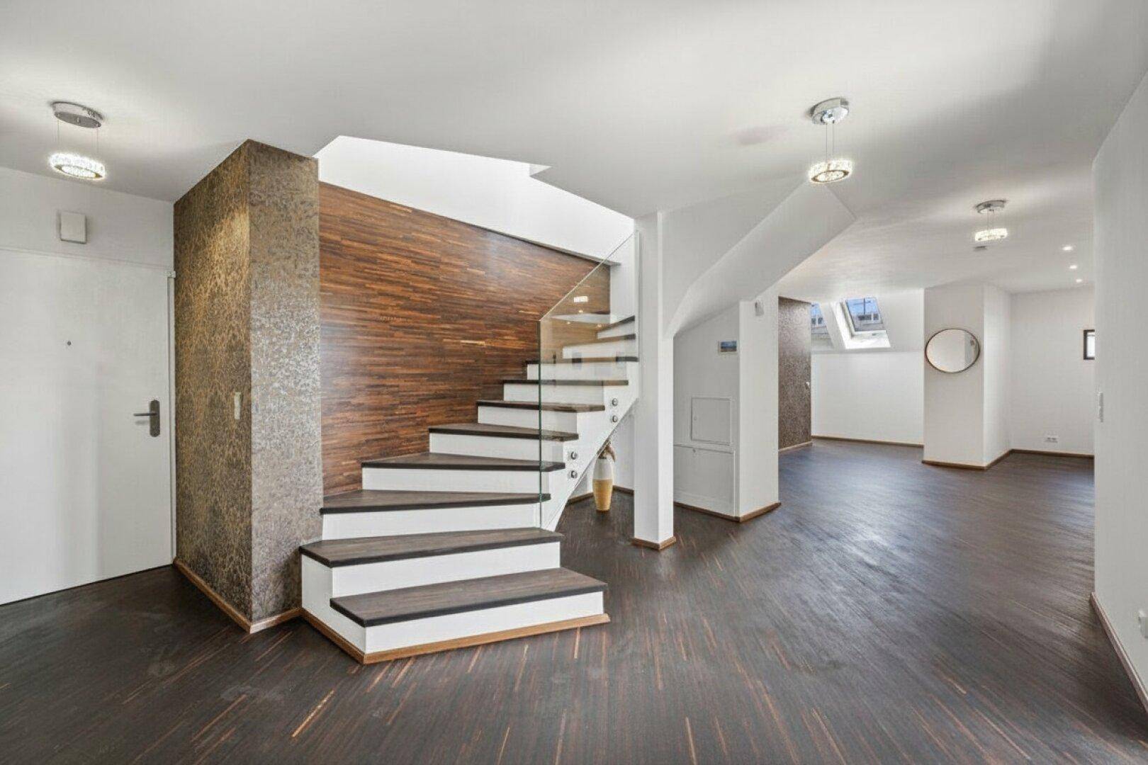 Moderner Eingangsbereich mit eleganter Treppe, Glasgeländer und dunklem Holzboden.
