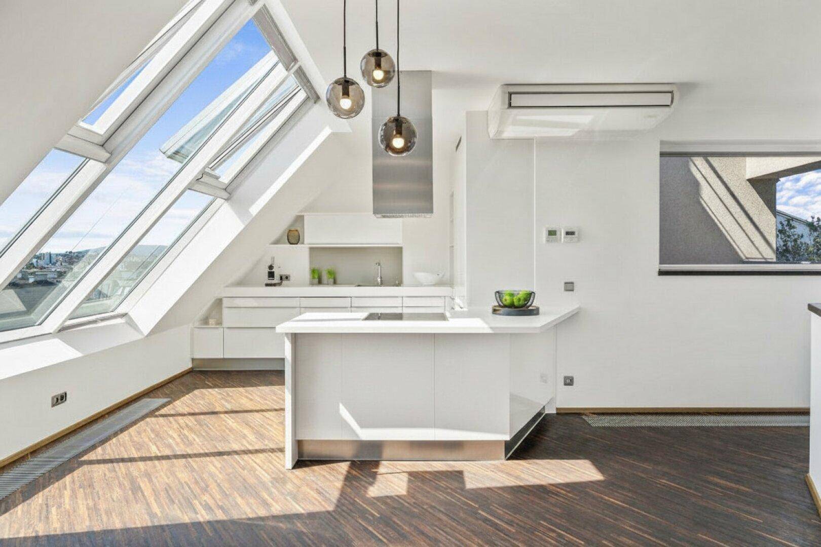 Moderne weiße Küche mit Dachschrägenfenstern, Kochinsel und Dunstabzugshaube in einem hellen Raum.