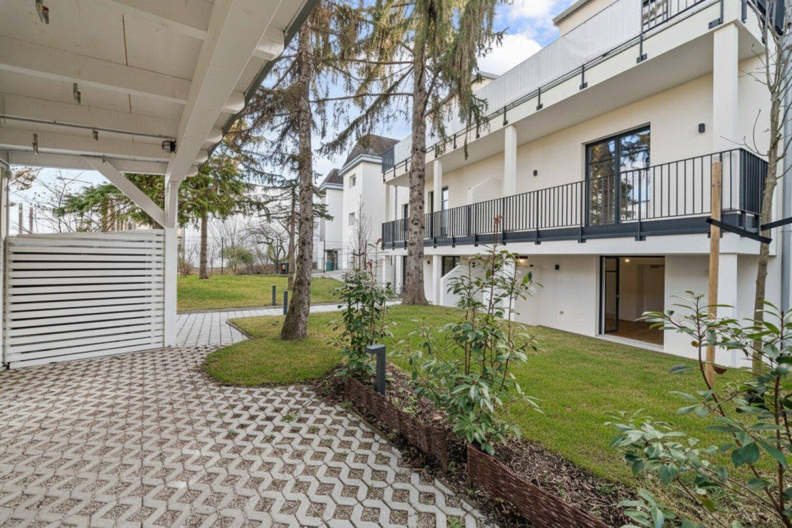 Außenansicht des Gebäudes mit Carport, gepflegtem Rasen und Balkonen in grüner Umgebung.