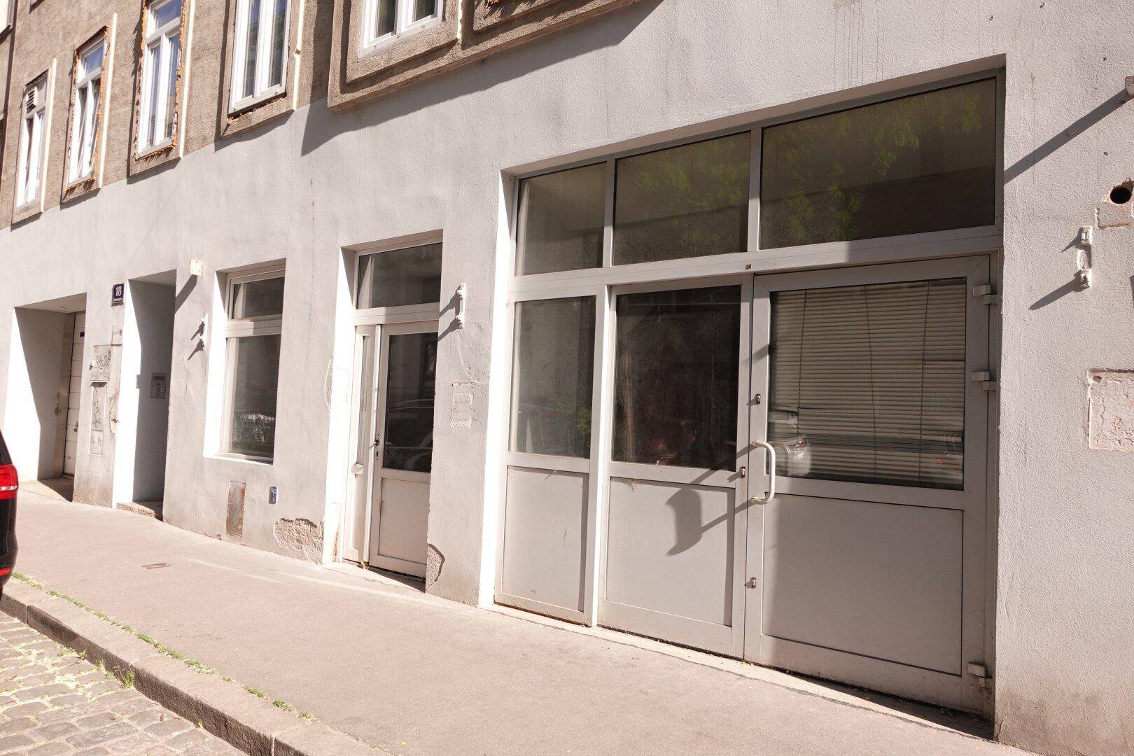 Straßenansicht der Gebäudefassade mit mehreren Eingängen und großen Fenstern im Erdgeschoss.