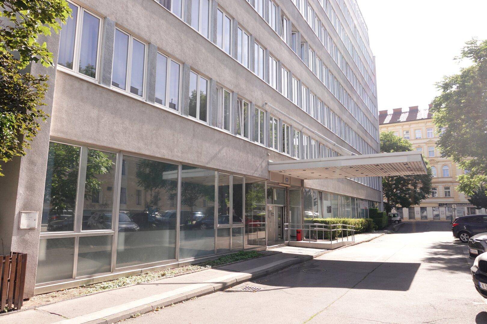 Moderne Gebäudefassade mit großen Fenstern und einem überdachten Eingangsbereich an der Straße.